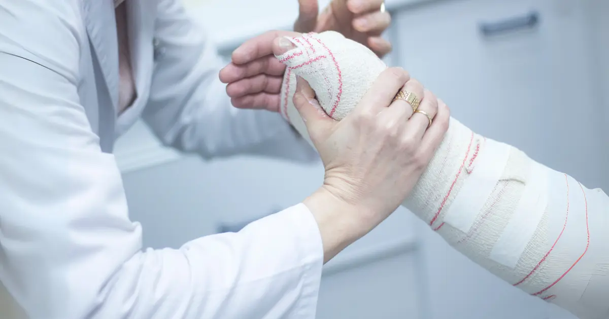 Médico enfaixando o braço de um paciente com lesão, representando cuidados médicos e direitos relacionados ao auxílio-doença.