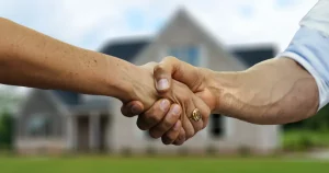 Imagem de um aperto de mãos em frente a uma casa, representando a regularização de imóveis por meio de diferentes tipos de usucapião.